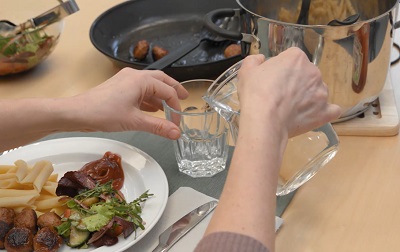 En person häller upp vatten i ett glas vid ett dukat bord